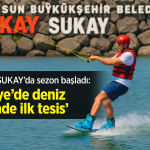 Kasklı ve kırmızı can yelekli sporcu, Karadeniz üzerinde su kayağı yaparken arka planda “Samsun Büyükşehir Belediyesi SUKAY” tabelası görünüyor.